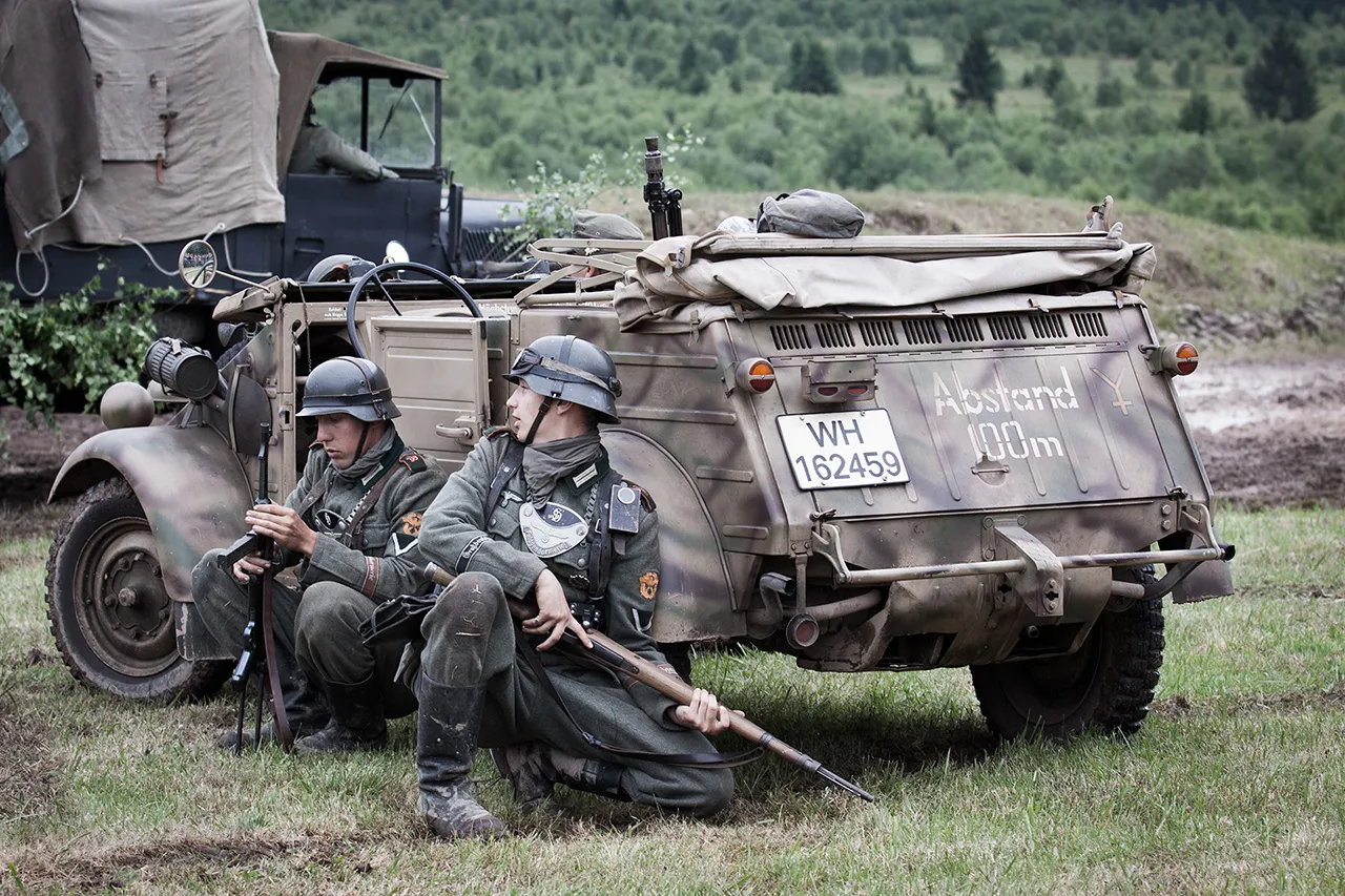 Vojáci v dobových německých uniformách kryjící se za historickým vozidlem Kübelwagen, rekonstrukce bitvy, akce Bahna