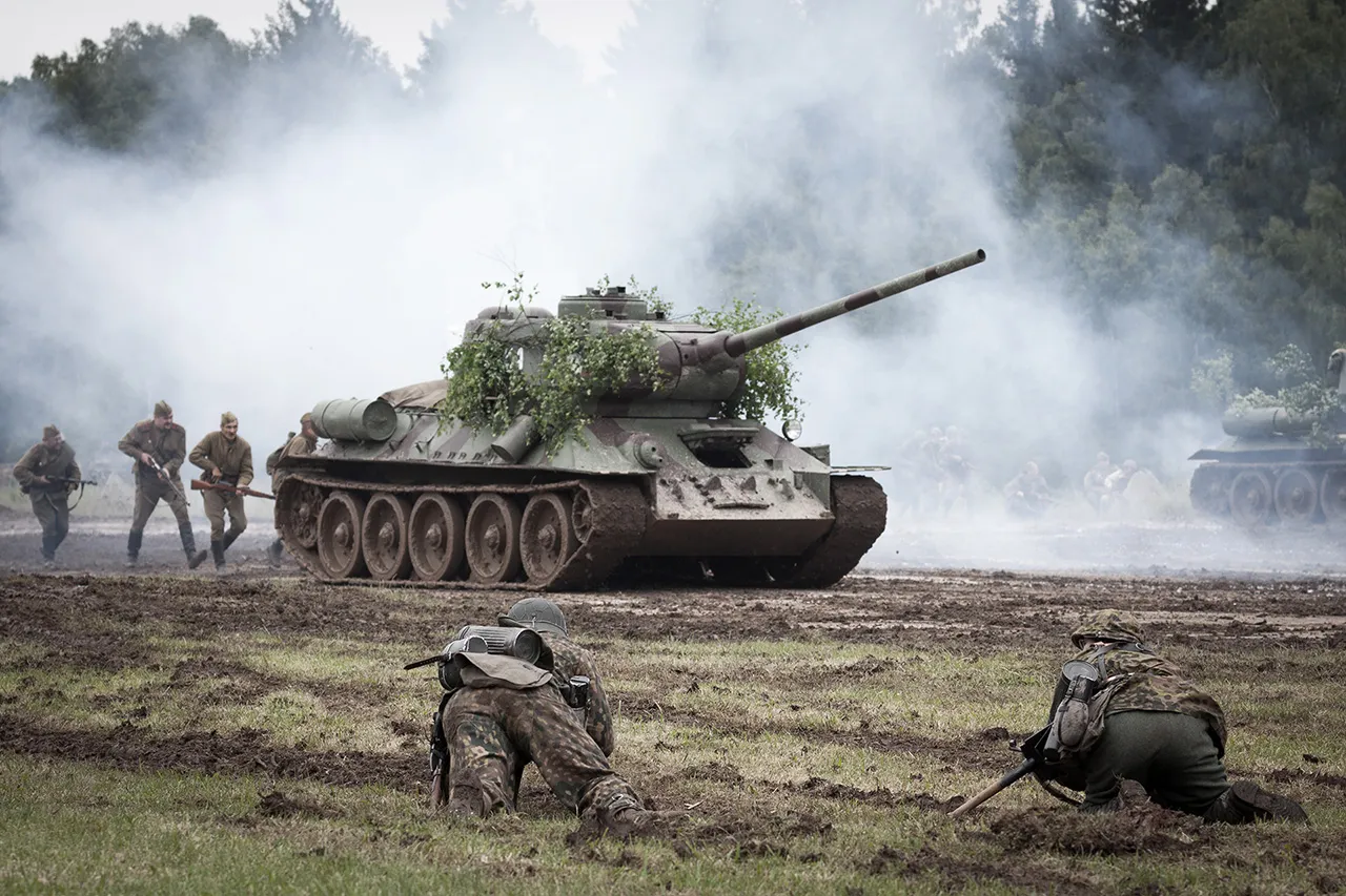 Sovětský tank T-34/85 v postupu za doprovodu pěchoty, čelící obraně v blátivém terénu, rekonstrukce bitvy, akce Bahna.