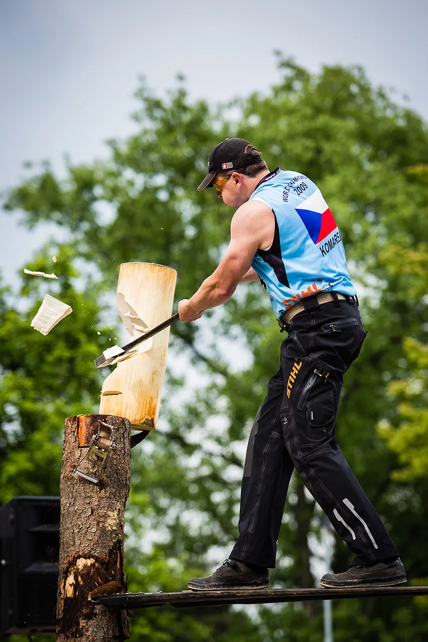 Český závodník STIHL Timbersports v dresu s trikolórou seká obouruční sekerou do stojící klády při disciplíně Springboard, přičemž stojí na úzkém prkně.