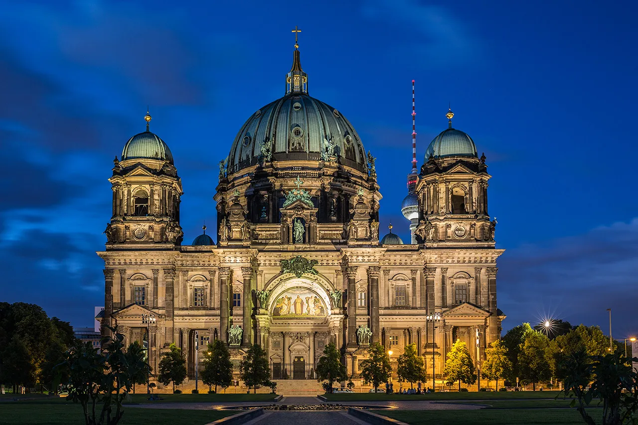 Detailní pohled na osvětlenou Berlínskou katedrálu (Berliner Dom) s televizní věží v pozadí.