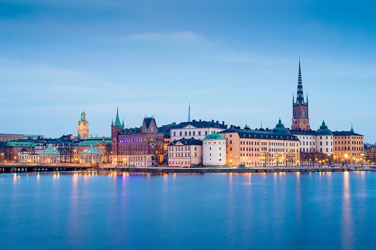 Pohled na historické centrum Stockholmu (Gamla Stan) přes vodní hladinu během klidného večera.