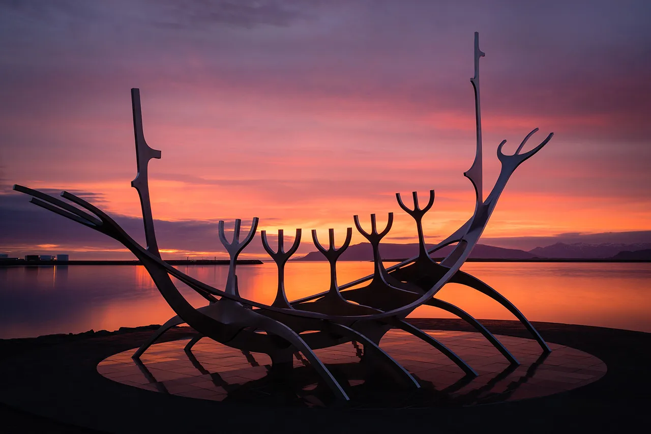 Ocelová skulptura Sun Voyager v Reykjavíku na pozadí barevného západu slunce u moře.