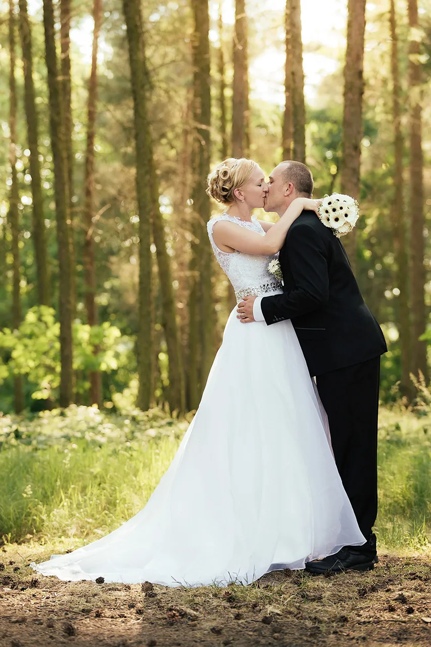 Novomanželé, nevěsta a ženich dávající si polibek v lese
